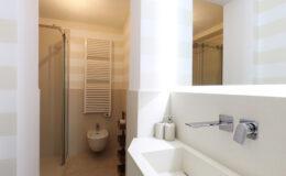 Modern bathroom featuring a sleek design with a walk-in shower, minimalist sink, and stylish fixtures. Light-colored walls with subtle stripes create a spacious feel, complemented by a towel radiator and contemporary accessories.