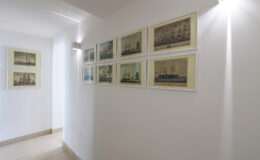 Gallery wall displaying vintage maritime artwork in a well-lit hallway, featuring framed prints of ships and nautical scenes.