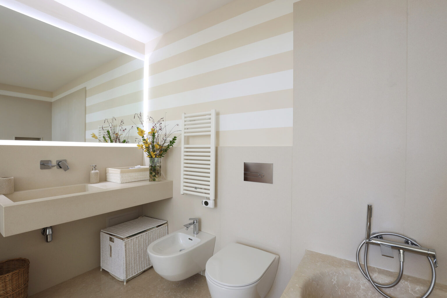 Modern bathroom interior featuring a stylish sink, toilet, bidet, and a mirror with ambient lighting. The walls are adorned with soft striped patterns, and a decorative plant adds a touch of elegance to the space. | Only on SopranoVillas