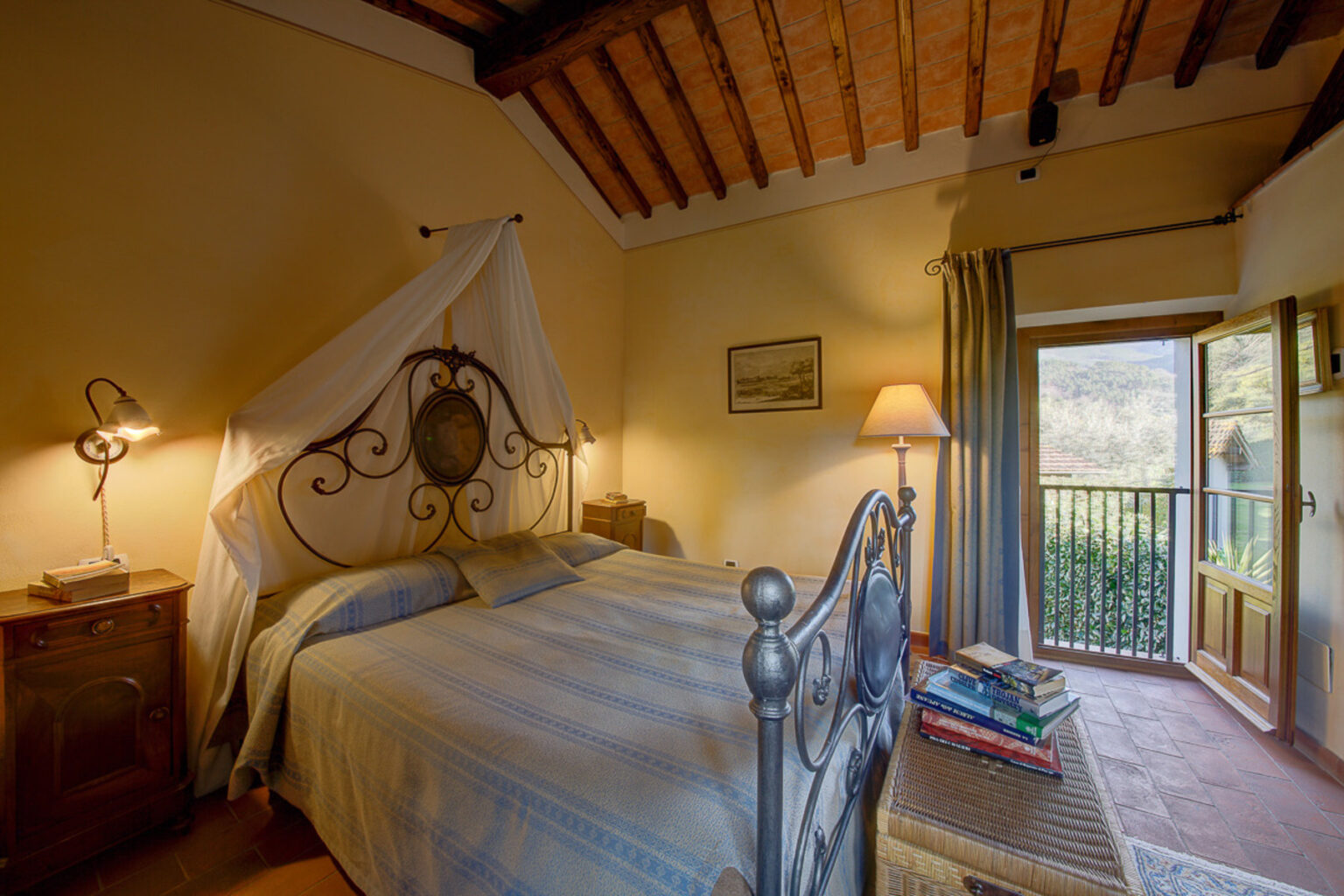 Cozy bedroom with a wrought iron bed, soft linens, and a canopy, featuring rustic wooden beams and a balcony with scenic views. Ideal for relaxation and comfort. | Only on SopranoVillas