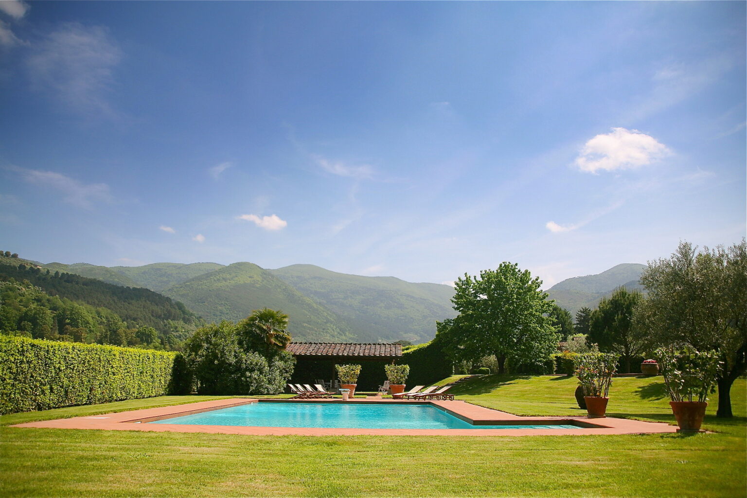 Scenic outdoor swimming pool surrounded by lush greenery and mountains under a clear blue sky, ideal for relaxation and leisure activities. | Only on SopranoVillas