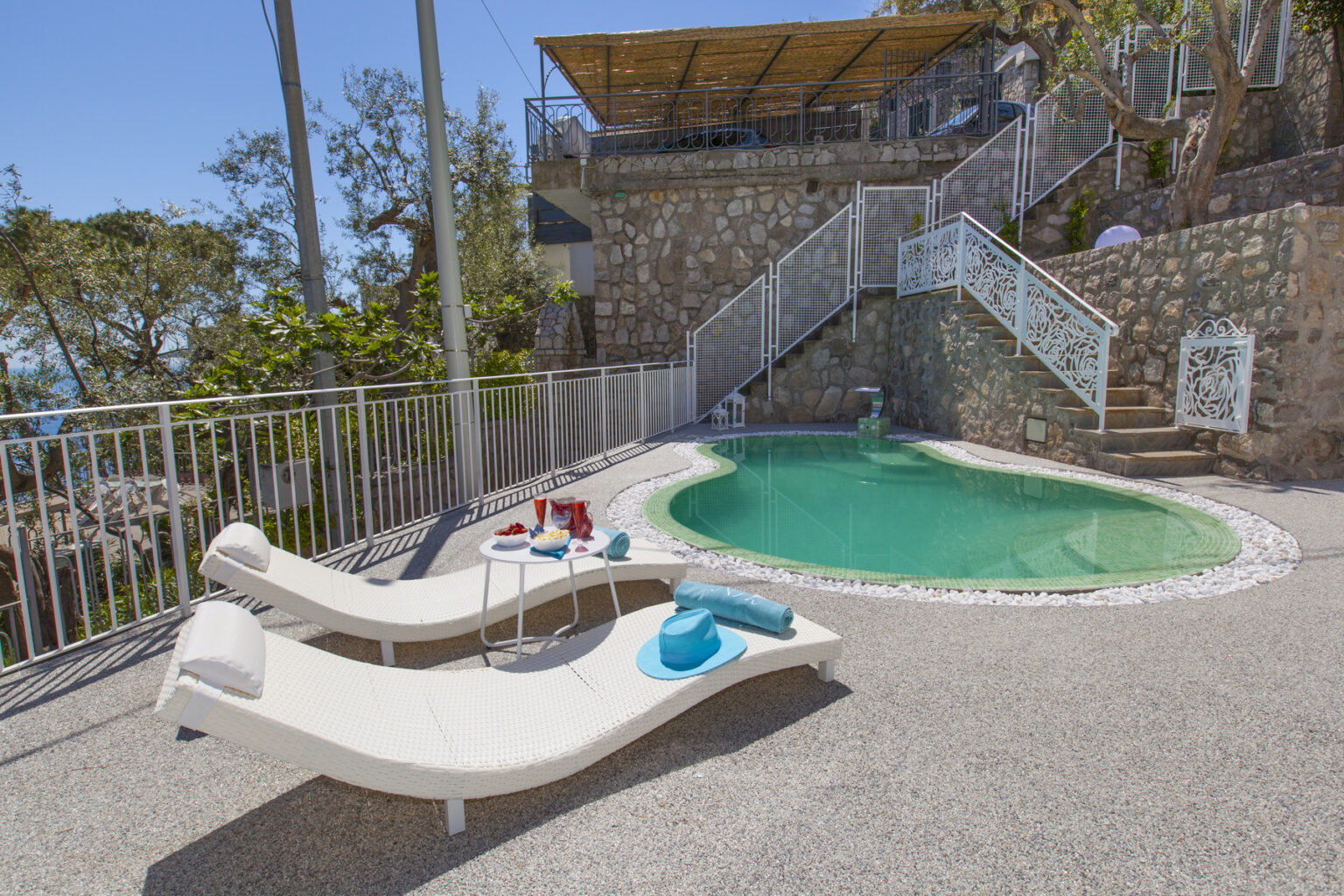 Lounge chairs by a private pool surrounded by a stone wall and lush greenery, ideal for relaxation in a picturesque outdoor setting. | Only on SopranoVillas