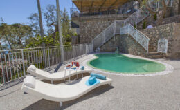 Lounge chairs by a private pool surrounded by a stone wall and lush greenery, ideal for relaxation in a picturesque outdoor setting.