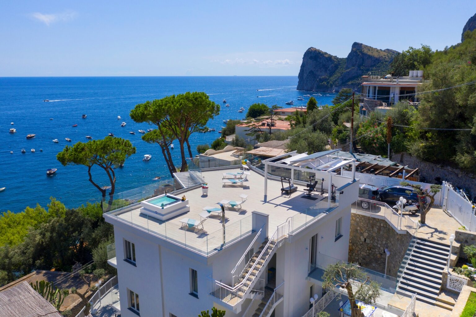 Luxury coastal villa with a rooftop terrace, overlooking the blue sea and boats, surrounded by lush greenery and rocky cliffs. Ideal for relaxation and stunning views. | Only on SopranoVillas