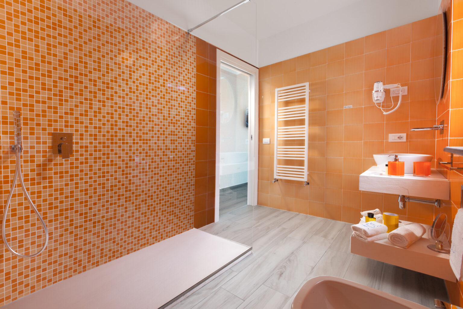 Modern bathroom with vibrant orange tiled walls, walk-in shower, and sleek fixtures, featuring a towel radiator and minimalist sink area. Perfect for contemporary home design inspiration. | Only on SopranoVillas