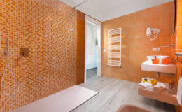 Modern bathroom with vibrant orange tiled walls, walk-in shower, and sleek fixtures, featuring a towel radiator and minimalist sink area. Perfect for contemporary home design inspiration.