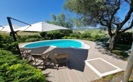 Scenic outdoor pool area with lounge chairs, umbrellas, and lush greenery overlooking rolling hills under a clear blue sky. Perfect for relaxation and enjoying nature.