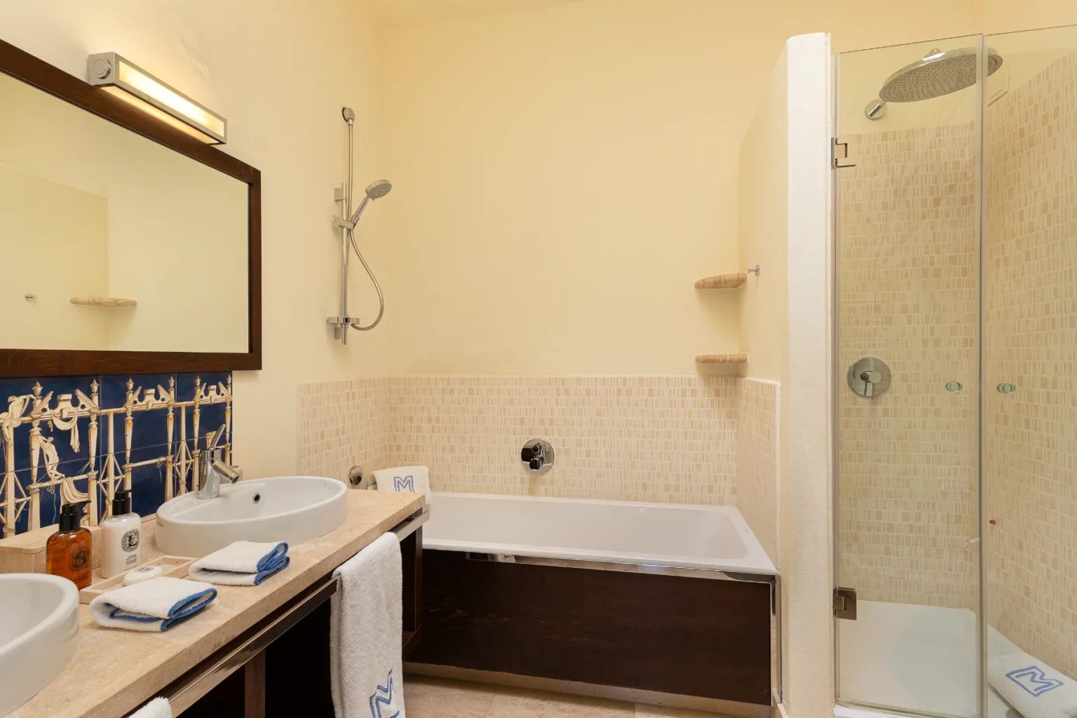 Modern bathroom featuring a glass shower, a bathtub, dual sinks with stylish fixtures, and decorative tile accents. Soft lighting and neutral tones create a relaxing atmosphere. | Only on SopranoVillas