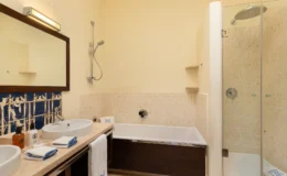 Modern bathroom featuring a glass shower, a bathtub, dual sinks with stylish fixtures, and decorative tile accents. Soft lighting and neutral tones create a relaxing atmosphere.