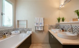 Modern bathroom interior featuring a freestanding bathtub, double sinks, and stylish mosaic tiles. Soft lighting highlights the elegant design, complemented by plush towels and decorative plants. The space exudes a clean and contemporary aesthetic.