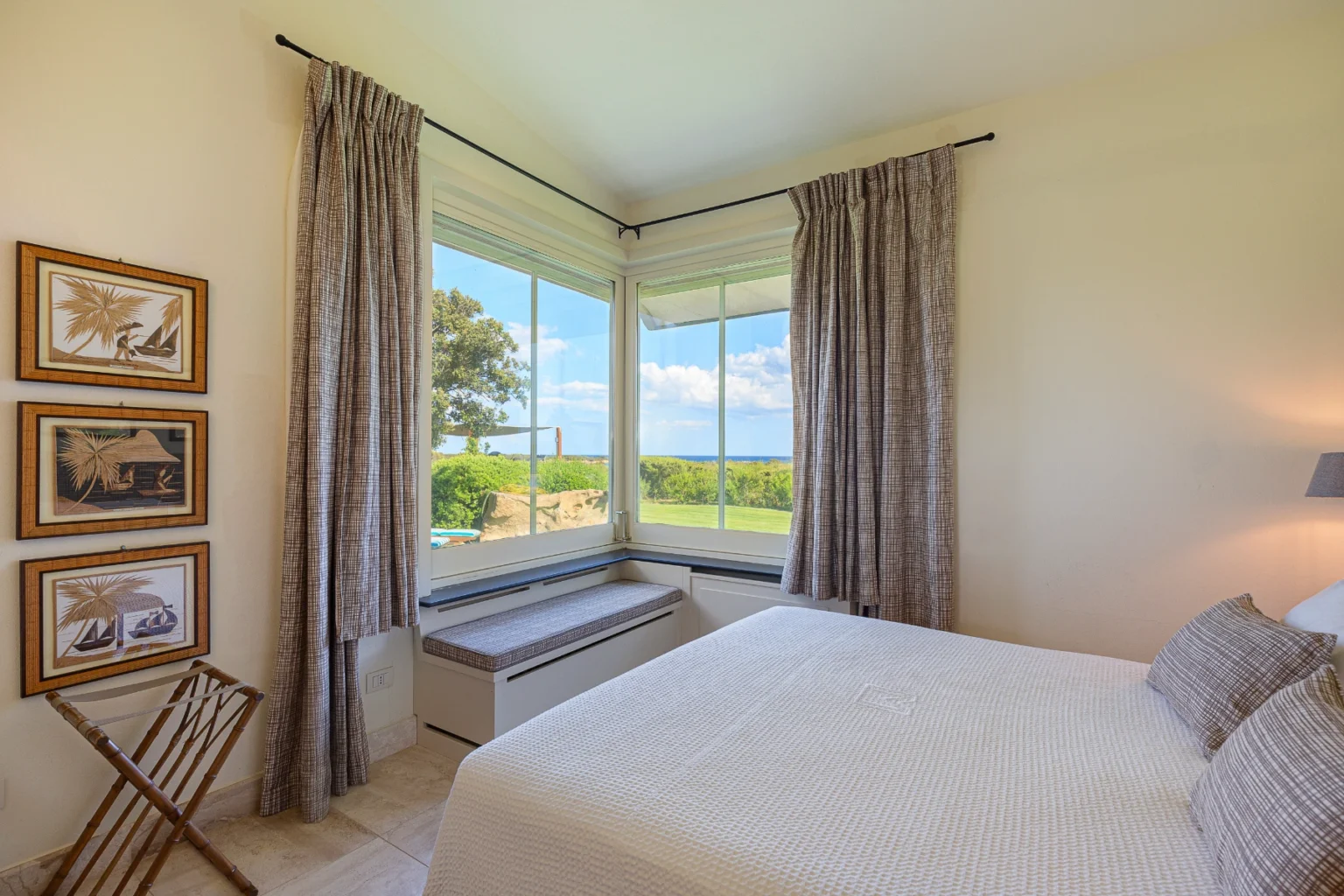Cozy bedroom featuring a large window with scenic views, soft bedding, and stylish curtains, complemented by framed artwork on the wall and a comfortable seating area by the window. | Only on SopranoVillas