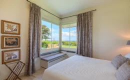 Cozy bedroom featuring a large window with scenic views, soft bedding, and stylish curtains, complemented by framed artwork on the wall and a comfortable seating area by the window.