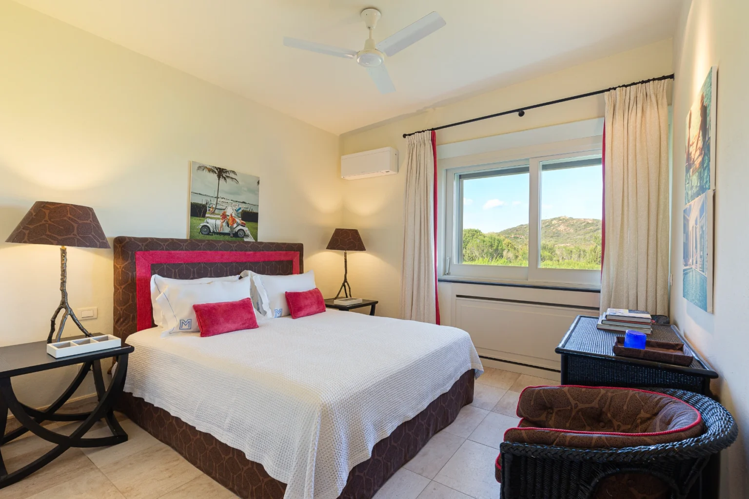 Cozy hotel bedroom featuring a king-sized bed with decorative pillows, bedside lamps, and a scenic window view. The room is adorned with light-colored walls, a ceiling fan, and stylish furniture, creating a relaxing atmosphere. | Only on SopranoVillas