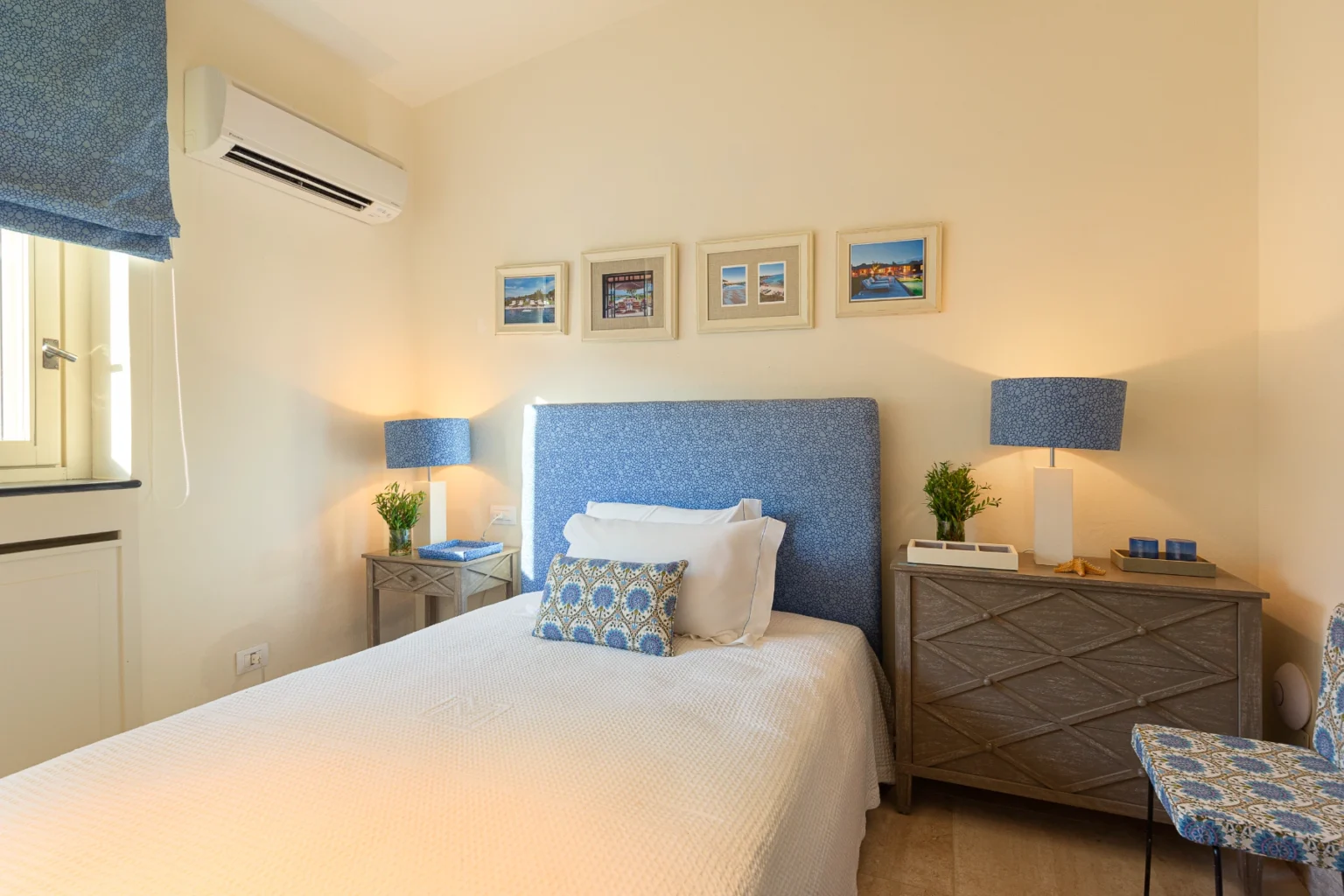 Cozy bedroom featuring a blue patterned headboard, bedside tables with matching lamps, and framed pictures on the wall. The room is well-lit with natural light from a window, creating a warm and inviting atmosphere. | Only on SopranoVillas