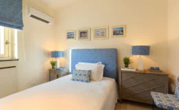 Cozy bedroom featuring a blue patterned headboard, bedside tables with matching lamps, and framed pictures on the wall. The room is well-lit with natural light from a window, creating a warm and inviting atmosphere.