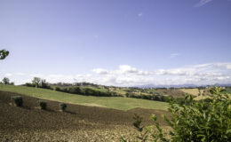 Scenic view of rolling hills and farmland under a clear blue sky, showcasing a picturesque village in the distance surrounded by lush greenery and plowed fields. Ideal for nature enthusiasts and landscape photography.
