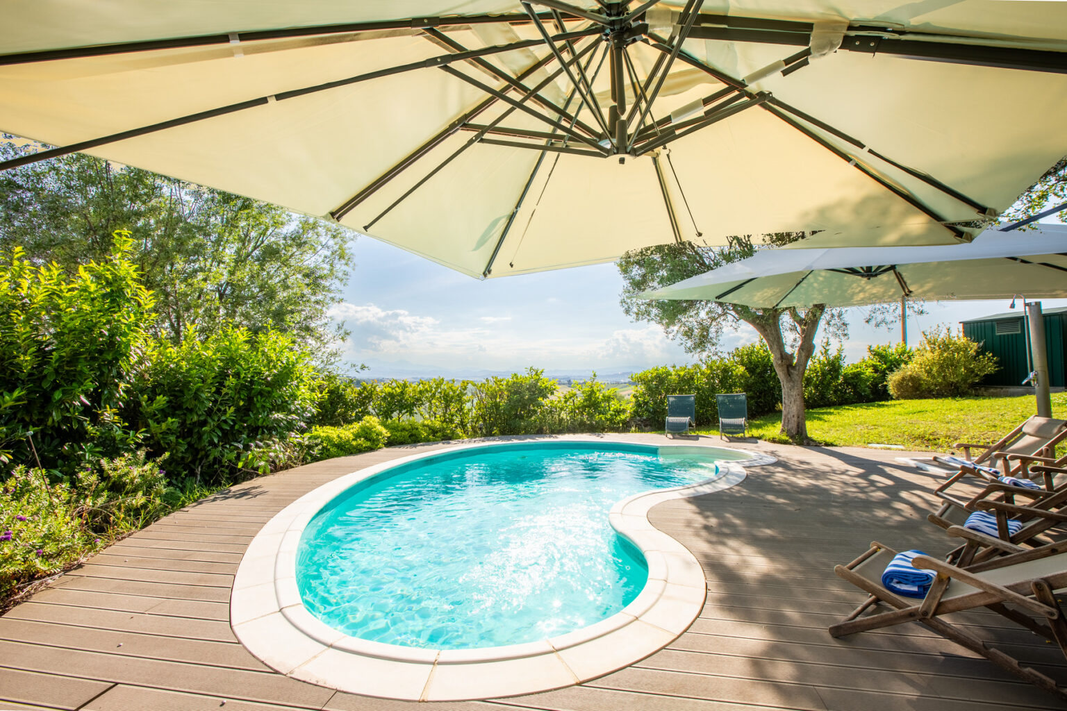Cozy outdoor pool surrounded by lush greenery and sun loungers, with a large umbrella providing shade, ideal for relaxation and leisure. | Only on SopranoVillas
