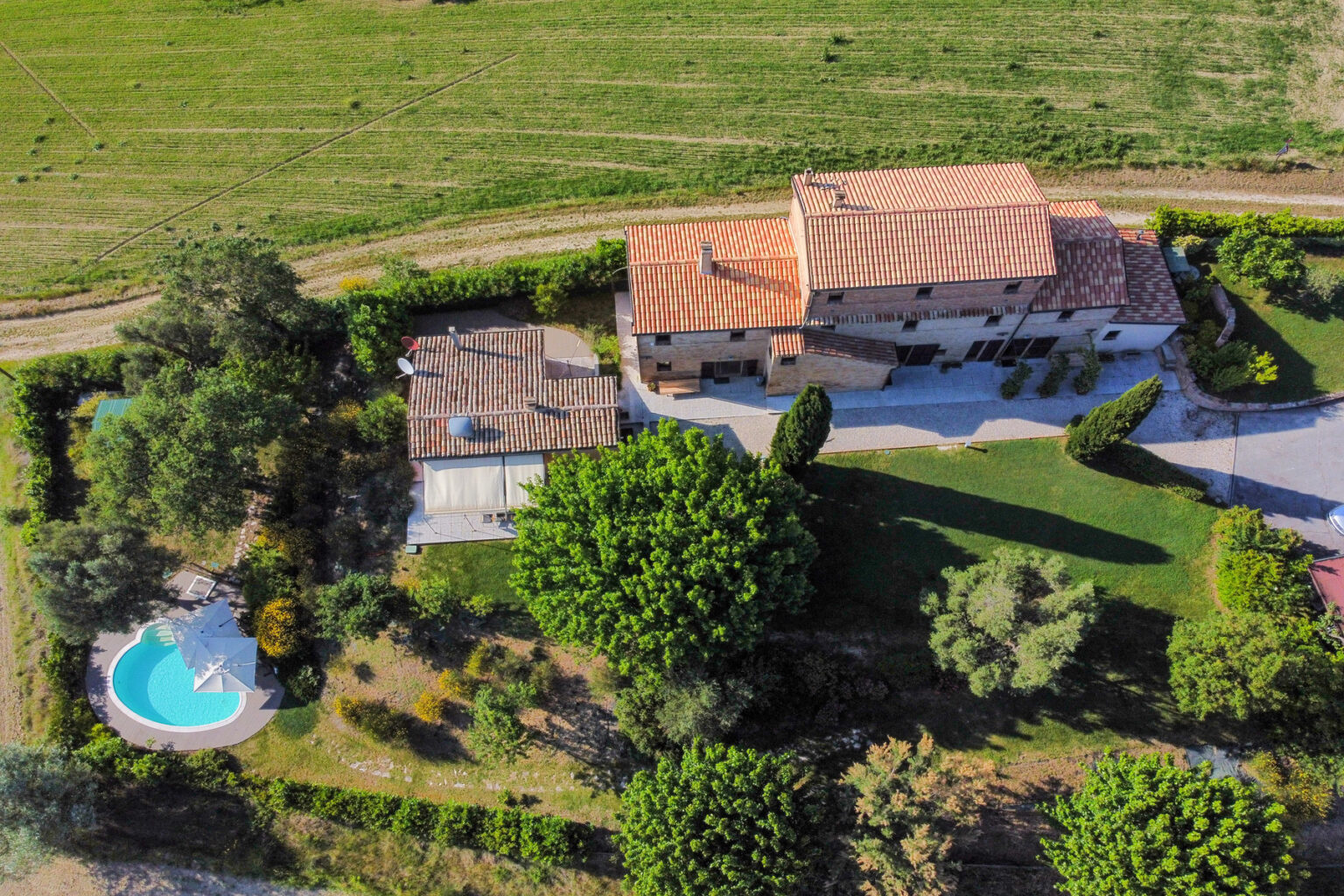 Aerial view of a spacious countryside villa with a pool, surrounded by lush greenery and a well-maintained lawn. The property features a rustic design and is situated in a serene landscape. | Only on SopranoVillas