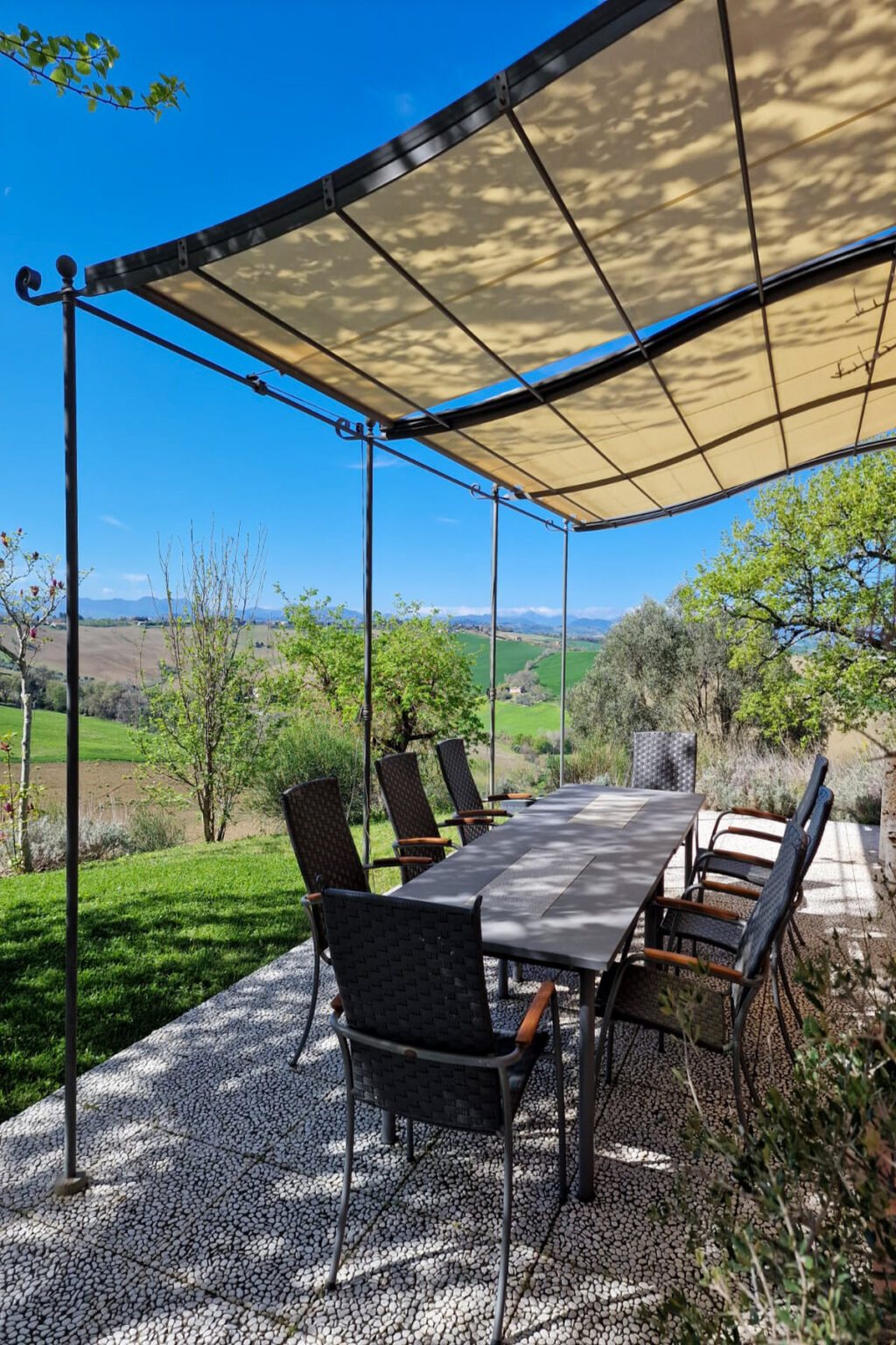 Outdoor dining area with a long table and chairs under a canopy, overlooking lush green fields and distant mountains on a clear day. | Only on SopranoVillas