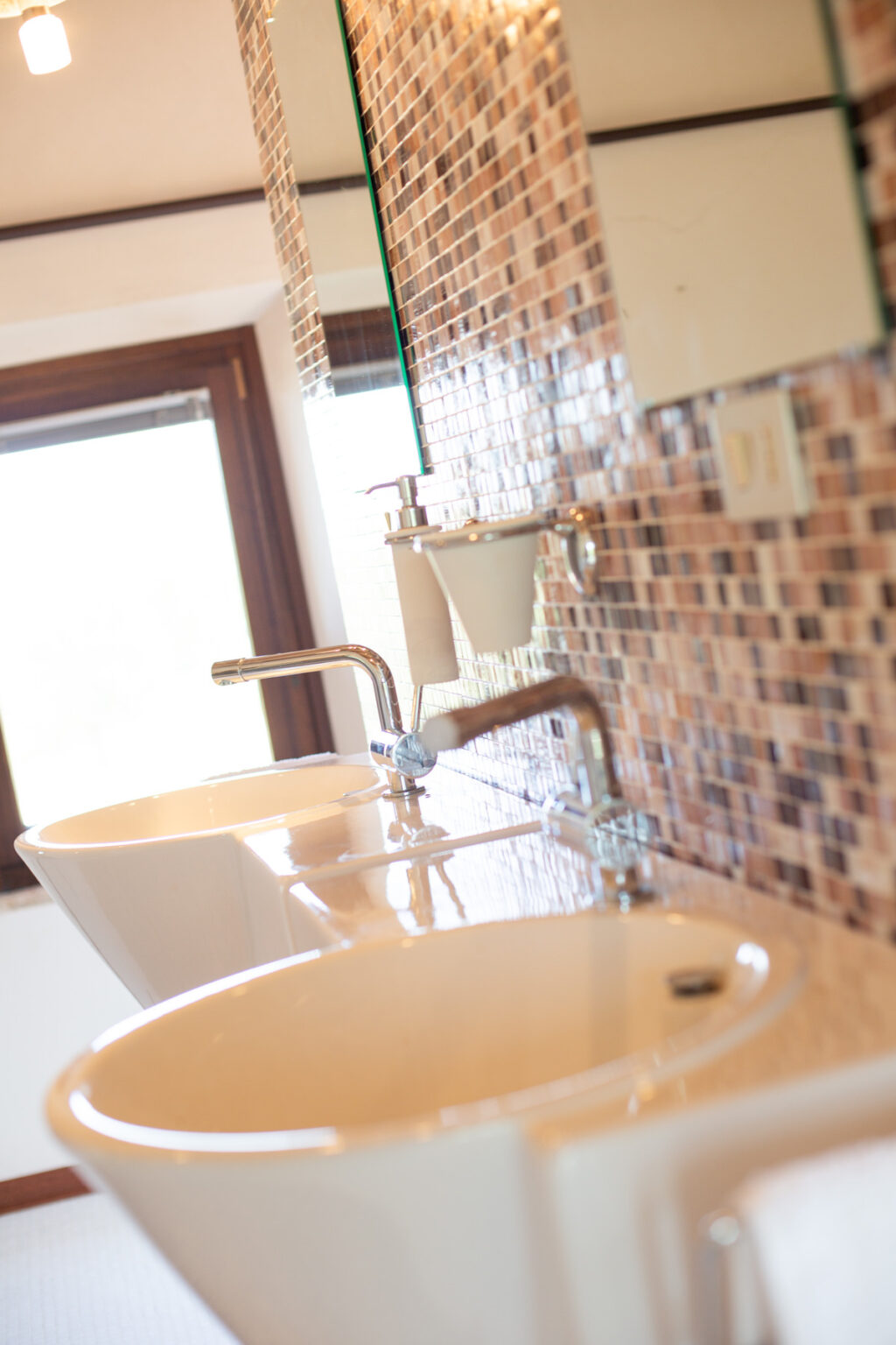 Modern bathroom with two white sinks, stylish chrome faucets, and a mosaic tiled wall, showcasing a clean and elegant design. | Only on SopranoVillas