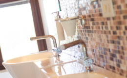Modern bathroom with two white sinks, stylish chrome faucets, and a mosaic tiled wall, showcasing a clean and elegant design.