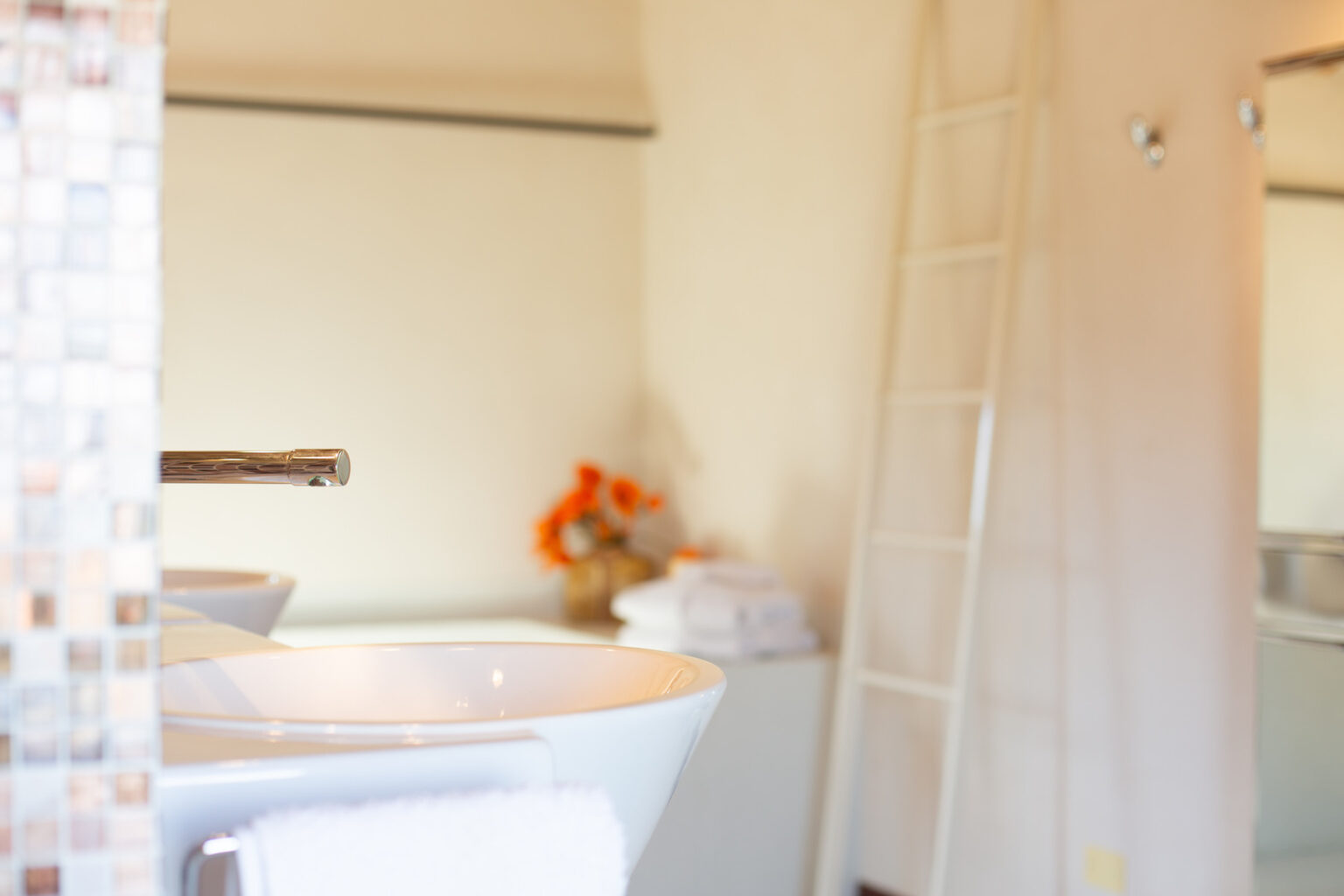 Modern bathroom interior featuring a sleek white sink with a chrome faucet, neatly arranged towels, and decorative orange flowers, creating a clean and inviting atmosphere. | Only on SopranoVillas