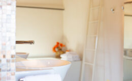 Modern bathroom interior featuring a sleek white sink with a chrome faucet, neatly arranged towels, and decorative orange flowers, creating a clean and inviting atmosphere.