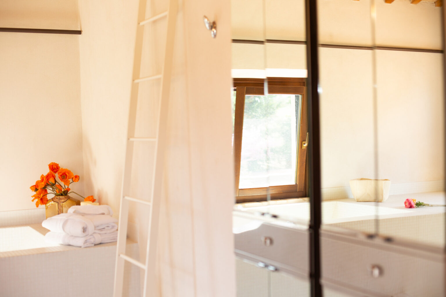 Bright and airy interior of a modern room featuring a wooden ladder, a window with natural light, and a bouquet of orange flowers on a white shelf, creating a cozy atmosphere. | Only on SopranoVillas