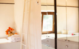 Bright and airy interior of a modern room featuring a wooden ladder, a window with natural light, and a bouquet of orange flowers on a white shelf, creating a cozy atmosphere.