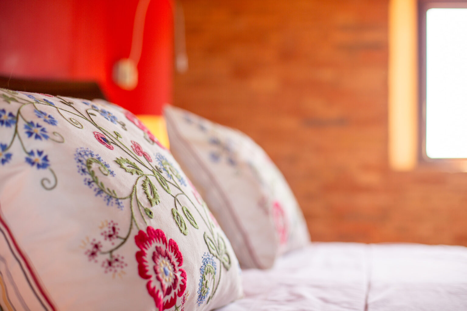 Close-up of embroidered decorative pillows on a neatly made bed, set against a warm wooden wall, creating a cozy and inviting bedroom atmosphere. | Only on SopranoVillas