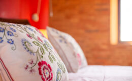 Close-up of embroidered decorative pillows on a neatly made bed, set against a warm wooden wall, creating a cozy and inviting bedroom atmosphere.