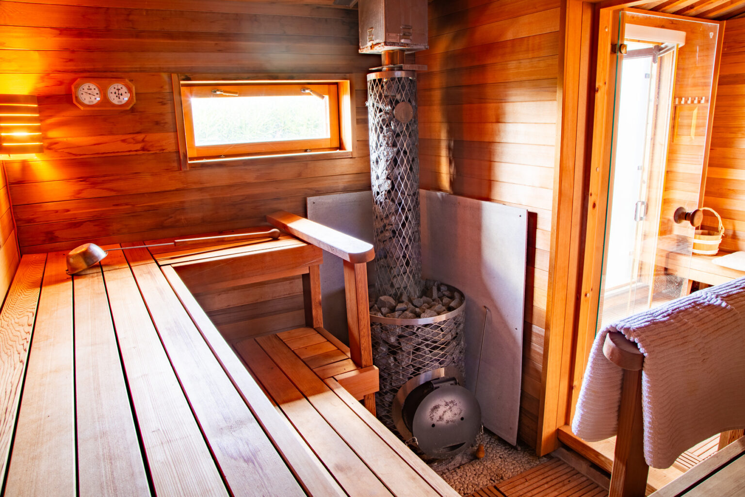 Interior of a modern sauna featuring wooden benches, a stone heater, and large windows for natural light, creating a relaxing atmosphere for wellness and rejuvenation. | Only on SopranoVillas
