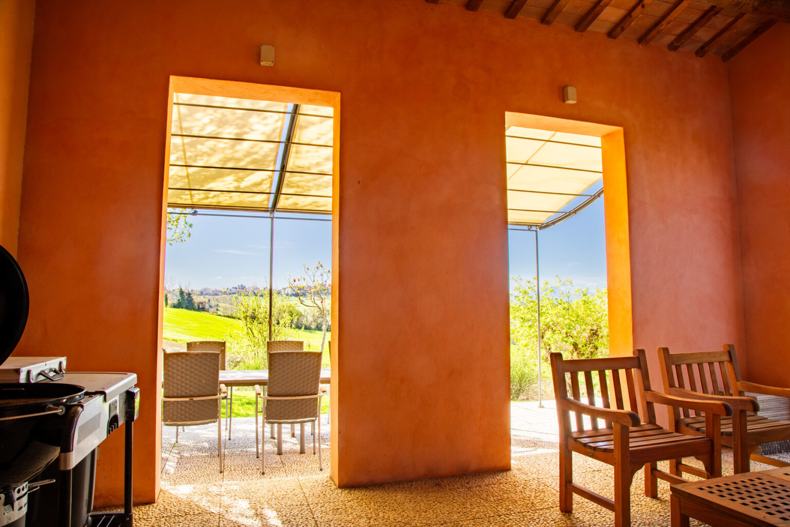 Interior view of a modern, orange-walled room featuring large windows that open to a scenic outdoor patio with seating. Natural light floods the space, highlighting the contemporary design and inviting atmosphere. | Only on SopranoVillas