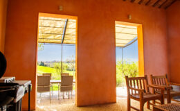 Interior view of a modern, orange-walled room featuring large windows that open to a scenic outdoor patio with seating. Natural light floods the space, highlighting the contemporary design and inviting atmosphere.