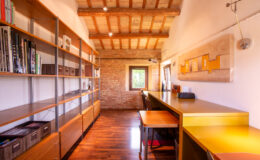 Modern office interior featuring wooden shelves filled with books, a sleek yellow desk, and exposed wooden beams on the ceiling, creating a bright and inviting workspace.