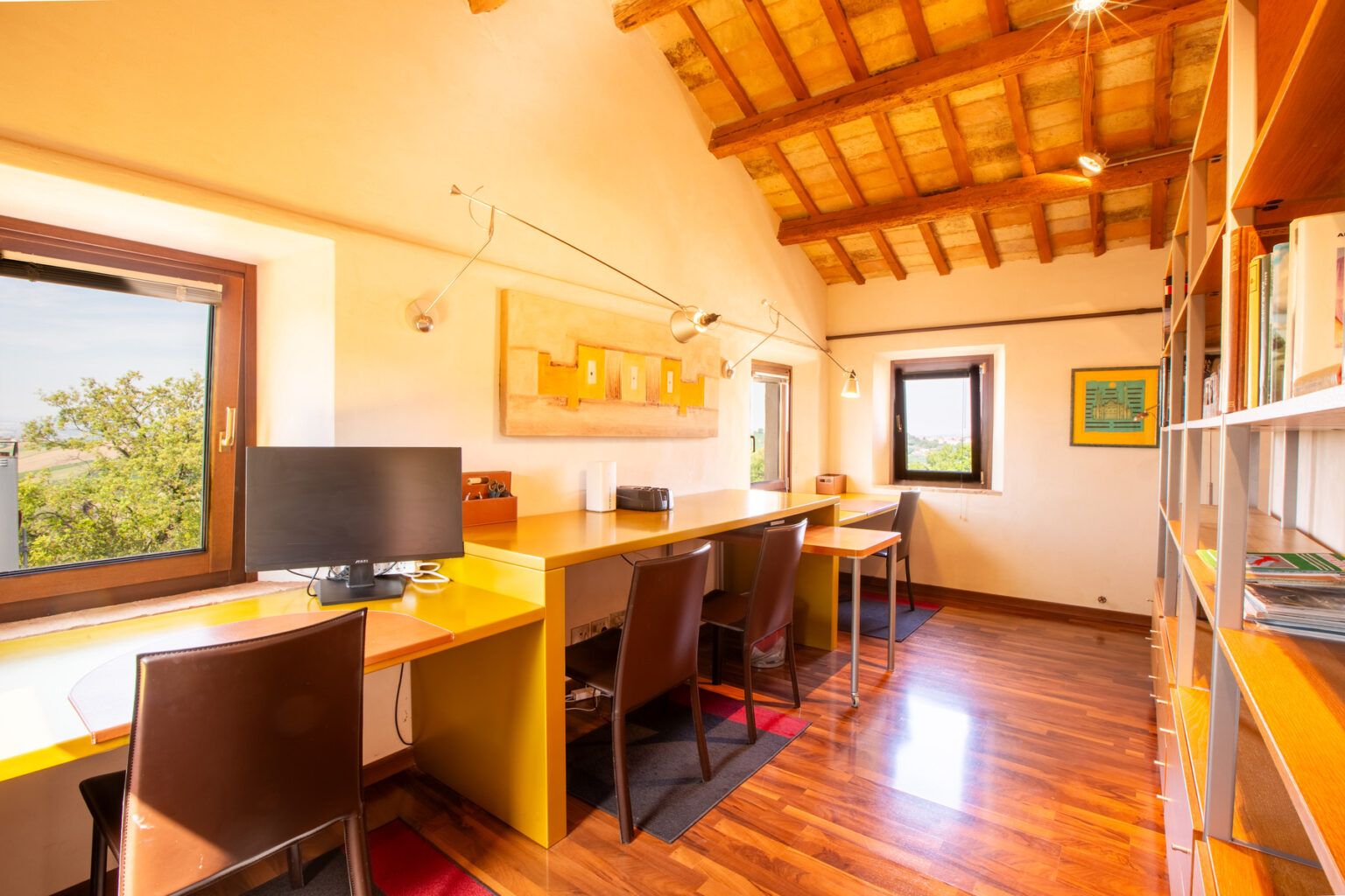 Bright and inviting home office with wooden beams, featuring two workstations, a computer, and bookshelves, overlooking a scenic view through large windows. Ideal for productivity and creativity. | Only on SopranoVillas