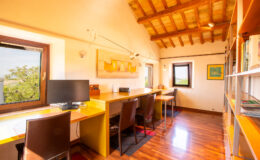 Bright and inviting home office with wooden beams, featuring two workstations, a computer, and bookshelves, overlooking a scenic view through large windows. Ideal for productivity and creativity.