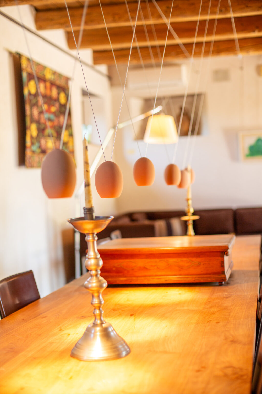 Modern dining room featuring a wooden table, a vintage candlestick holder, and a unique decorative element of hanging eggs. The warm lighting and rustic wooden beams create a cozy atmosphere, enhancing the stylish interior design. | Only on SopranoVillas
