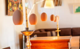 Modern dining room featuring a wooden table, a vintage candlestick holder, and a unique decorative element of hanging eggs. The warm lighting and rustic wooden beams create a cozy atmosphere, enhancing the stylish interior design.