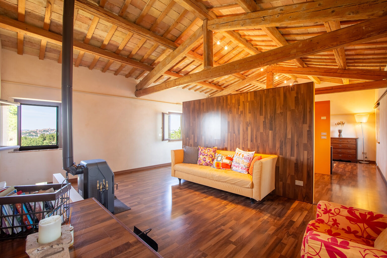 Cozy living room with wooden beams, featuring a stylish sofa, vibrant cushions, and a warm color palette, complemented by large windows that offer natural light and a view of the surroundings. | Only on SopranoVillas