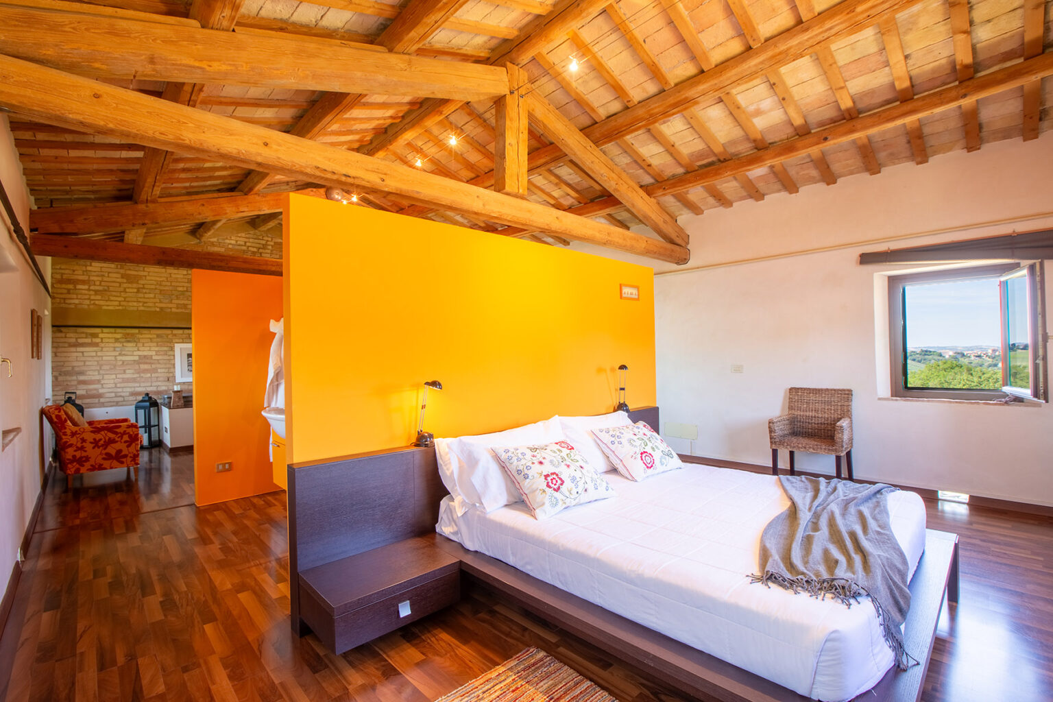 Modern bedroom with wooden beams, an orange accent wall, and a comfortable bed featuring decorative pillows, showcasing a cozy and inviting atmosphere. | Only on SopranoVillas