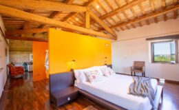 Modern bedroom with wooden beams, an orange accent wall, and a comfortable bed featuring decorative pillows, showcasing a cozy and inviting atmosphere.