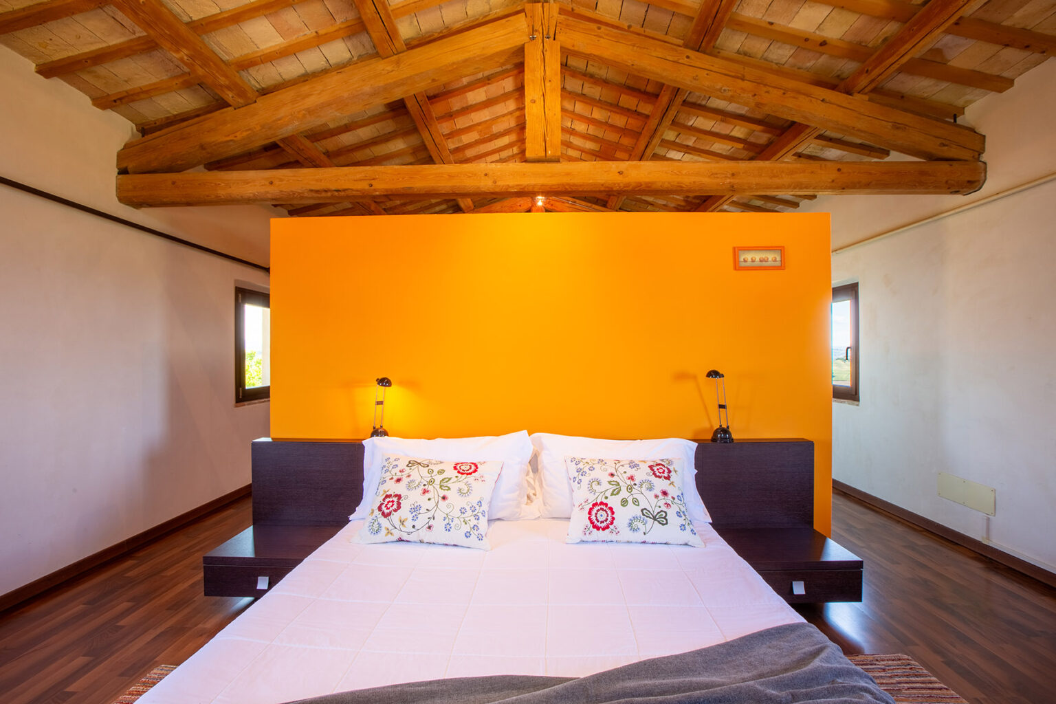 Cozy bedroom with a wooden ceiling, featuring a large bed with decorative pillows and an orange accent wall, creating a warm and inviting atmosphere. Ideal for relaxation and comfort. | Only on SopranoVillas