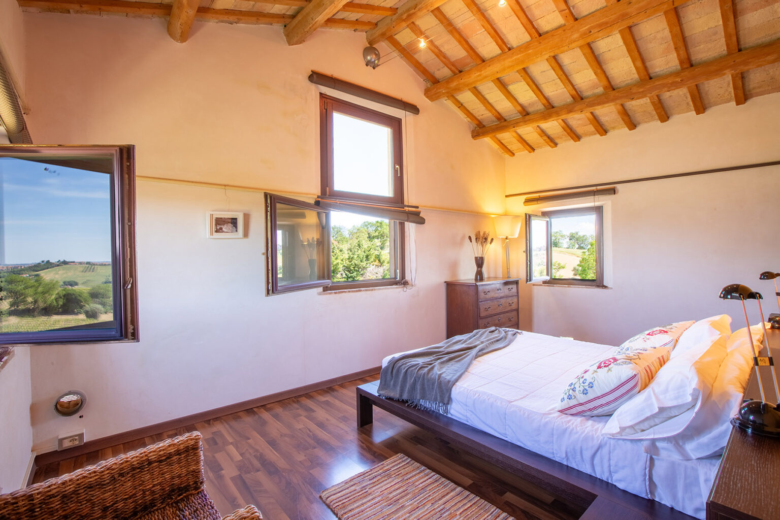 Bright and airy bedroom with wooden beams, large windows offering scenic views, a comfortable bed with decorative pillows, and a stylish wooden dresser. Ideal for a relaxing getaway. | Only on SopranoVillas