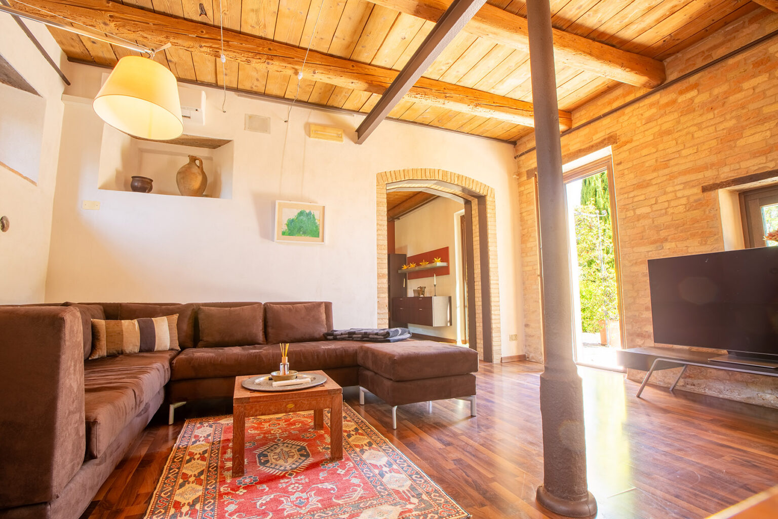 Cozy living room featuring a brown sectional sofa, wooden beams, and a flat-screen TV, with natural light streaming through the windows and a warm, inviting atmosphere. | Only on SopranoVillas