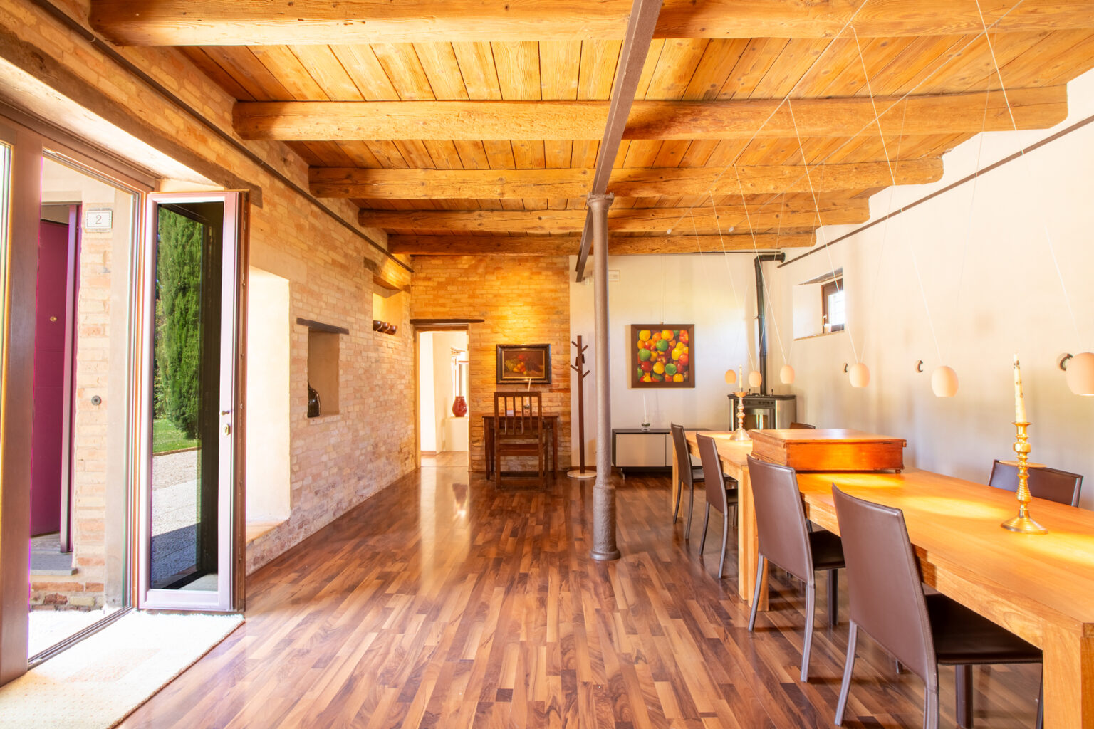Spacious dining area with wooden beams and polished hardwood floors, featuring a long dining table and modern decor, illuminated by natural light from large windows and doors. | Only on SopranoVillas
