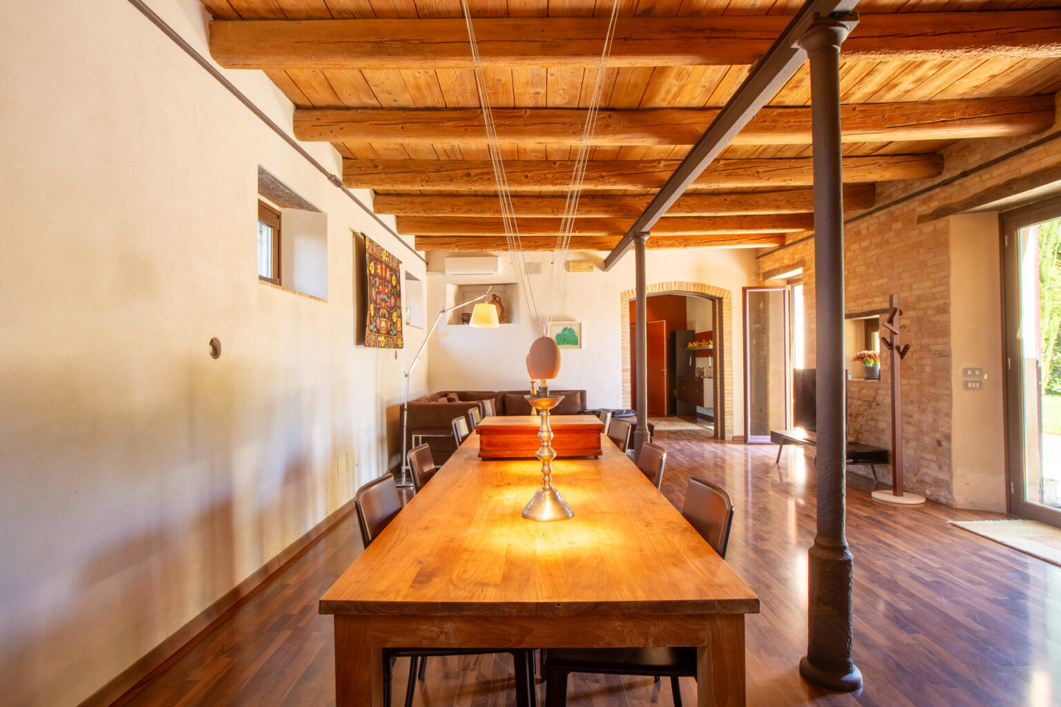 Spacious dining area featuring a wooden table, stylish chairs, and exposed wooden beams, with natural light streaming through large windows, creating a warm and inviting atmosphere. | Only on SopranoVillas