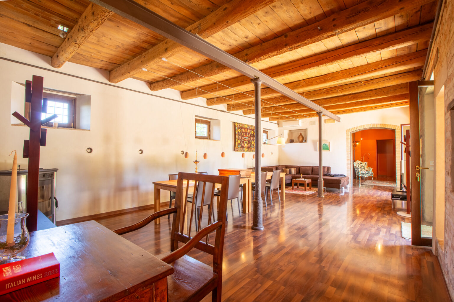 Spacious interior of a rustic dining area featuring wooden beams, polished hardwood floors, and a mix of tables and chairs, creating a warm and inviting atmosphere. | Only on SopranoVillas