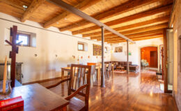 Spacious interior of a rustic dining area featuring wooden beams, polished hardwood floors, and a mix of tables and chairs, creating a warm and inviting atmosphere.