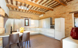 Modern kitchen with wooden beams and brick walls, featuring sleek white cabinetry, stainless steel appliances, and a dining area with a table and chairs.